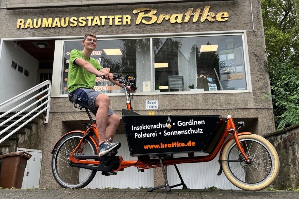 Knut Brattke auf dem Lastenrad vor seinem Ladenlokal mit dem Schriftzug Raumausstatter Brattke
